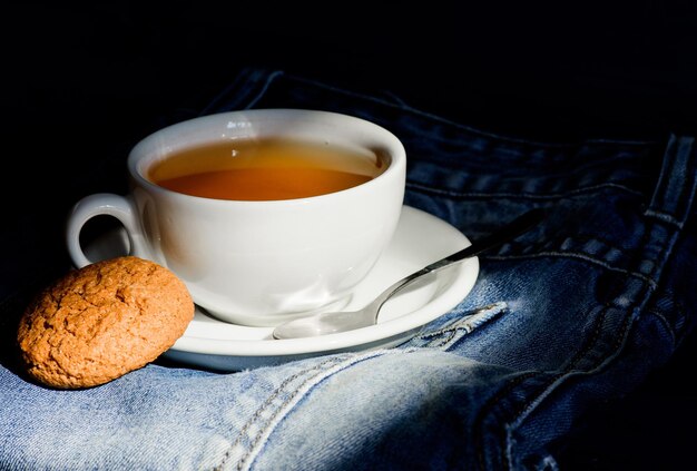 Hábitos saudáveis. Conceito de hora do chá. Copo caneca água quente e saquinho de chá. Caneca cheia de água fervente e saquinho de chá em fundo de jeans azul. Folha inteira verde ou preta de ervas. Processo de infusão de chá em uma caneca de cerâmica.