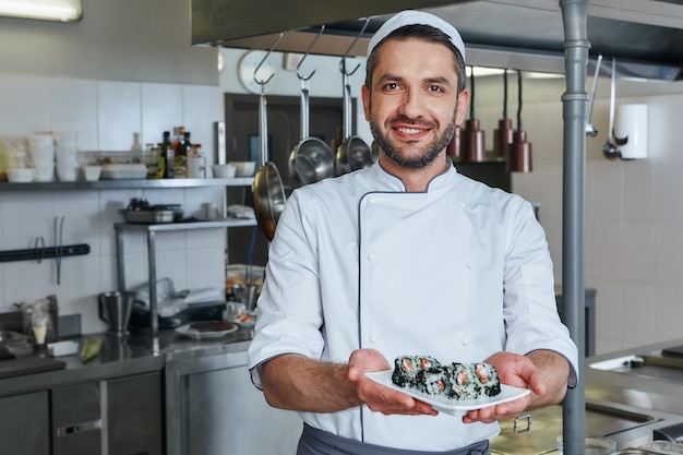 Habla con el retrato del gusto del chef alegre de pie con sushi japonés tradicional cocinado