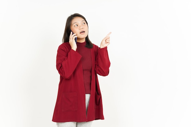 Hablando por teléfono inteligente y apuntando a un lado de la hermosa mujer asiática vestida con camisa roja