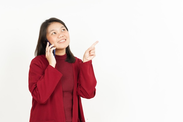 Hablando por teléfono inteligente y apuntando a un lado de la hermosa mujer asiática vestida con camisa roja