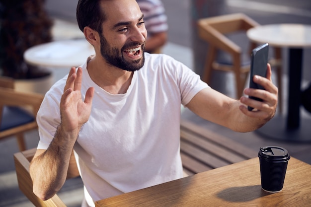 Hablando por teléfono inteligente, el hombre se sienta a la mesa en el café al aire libre de cerca