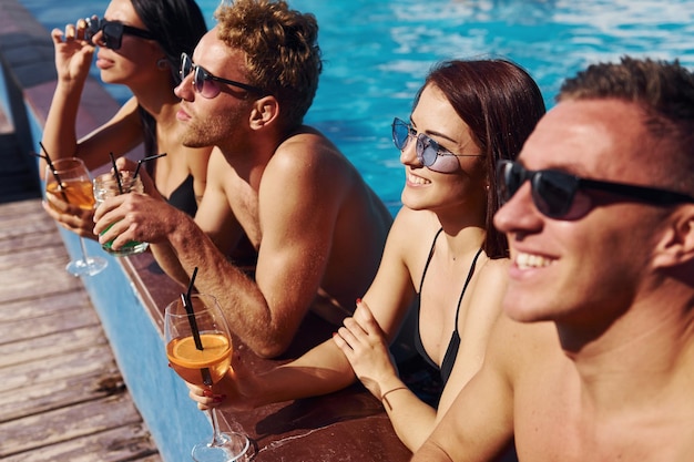 Hablar y beber Grupo de jóvenes felices divertirse en la piscina durante el día