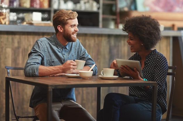 Foto Él la hace reír fotografía de una pareja joven usando una tableta digital juntos en una cita para tomar un café