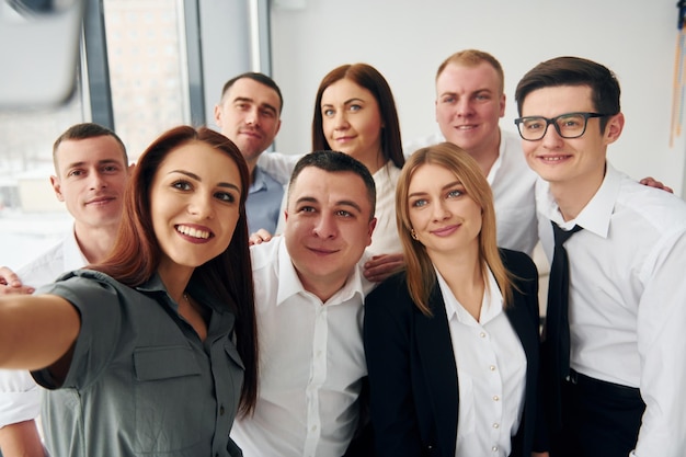 Hace una selfie de un grupo de personas con ropa formal oficial que está en el interior de la oficina