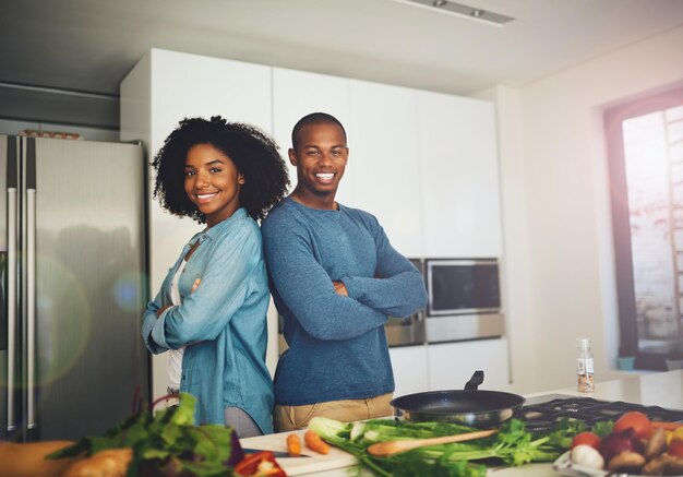 Hacemos el mejor equipo Retrato de una pareja joven alegre de pie juntos sobre una mesa llena de ingredientes que están a punto de usar para cocinar en la cocina de casa