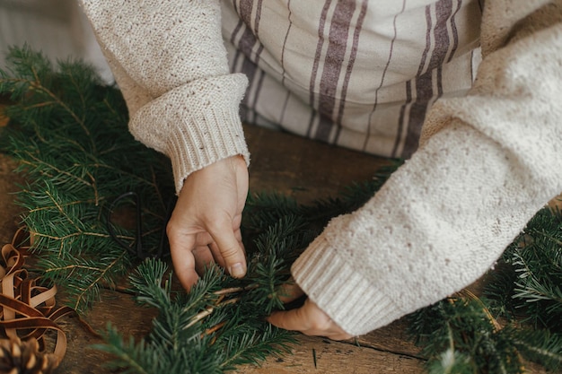 Hacer corona rústica de Navidad Manos de mujer sosteniendo ramas de abeto y haciendo corona en la mesa de madera