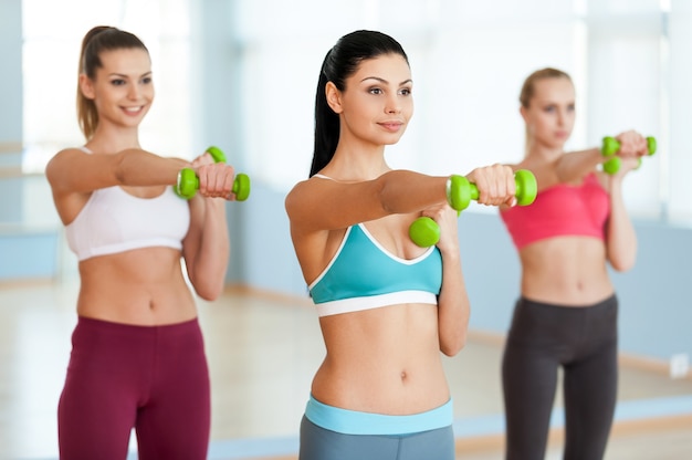 Hacer ejercicio con mancuernas. Tres hermosas mujeres jóvenes en ropa deportiva