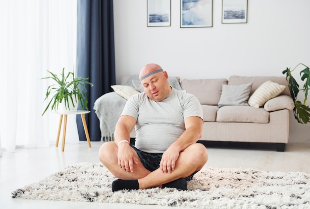 Hacer ejercicios de yoga Un hombre gracioso con sobrepeso vestido con ropa informal está en el interior de su casa