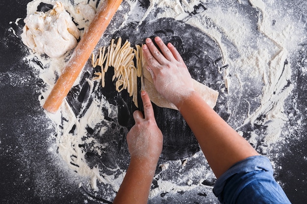 Foto hacer fideos caseros, espolvorear harina de trigo y cocinar manos. vista superior en pizarra o mesa.