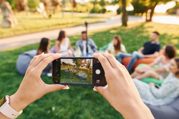 Hacer fotos usando un teléfono inteligente Grupo de jóvenes tienen una fiesta en el parque durante el día de verano