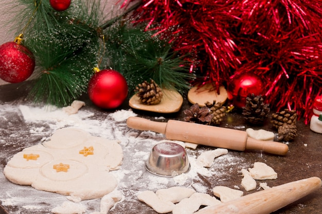 Hacer galletas navideñas, utensilios de cocina de madera, adornos navideños rojos, masa para hornear, molde para galletas