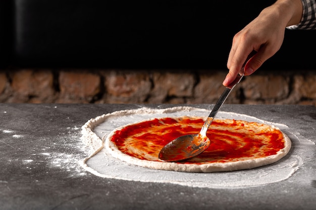 Hacer una pizza untando salsa de tomate sobre la masa sobre la superficie de hormigón gris