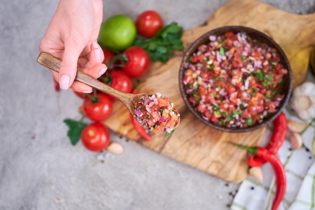 Hacer salsa dip salsa mujer mezclando ingredientes picados en tazón de madera