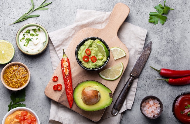 Hacer salsa de guacamole vegano verde saludable con aguacate fresco, lima, ají en la tabla de cortar de madera con un cuchillo viejo, fondo rústico de piedra, vista superior, primer plano. Salsa tradicional mexicana