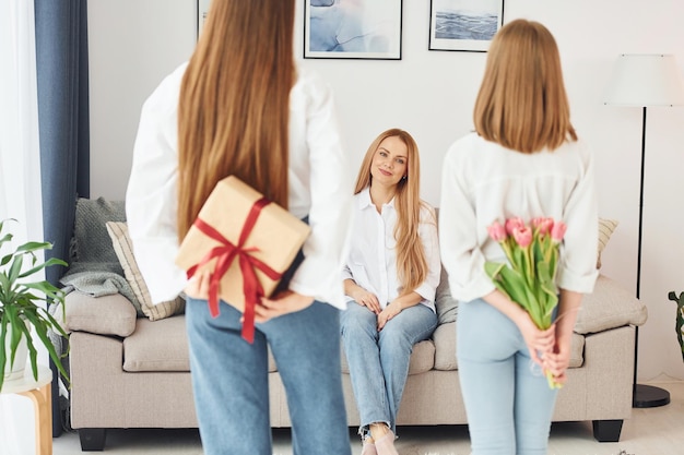 Hacer sorpresa con flores Joven madre con sus dos hijas en casa durante el día