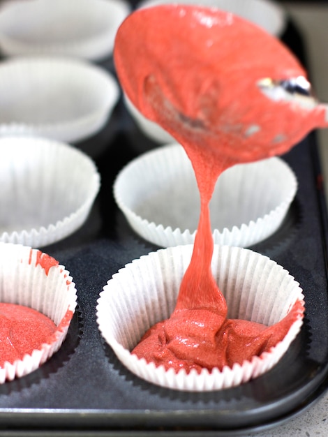 Haciendo cupcakes. Relleno por cucharada con formas de masa rosada para muffin.