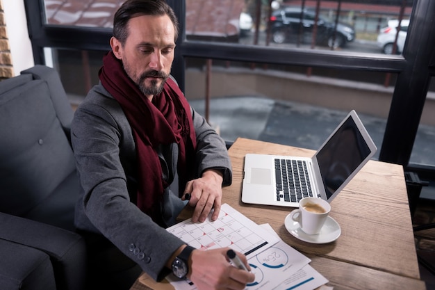 Haciendo el informe. Guapo trabajador autónomo trabajador sentado en la mesa y mirando el calendario mientras crea un horario de trabajo