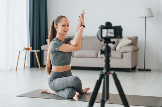 Haciendo lecciones en cámara Mujer joven con cuerpo delgado y ropa de yoga está en casa