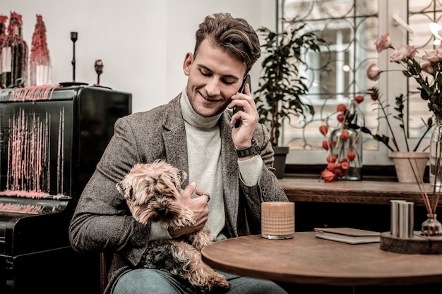 Haciendo una llamada. Un hombre sosteniendo un perro mientras hace una llamada telefónica.