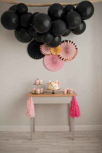 Haciendo una mesa dulce para un cumpleaños. Pastel gato y guirnalda de bolitas negras. Diseño rosa y negro.
