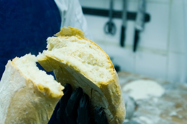 Haciendo pan ciabatta en la panadería. Un cocinero en guantes rompe el pan en dos mitades.