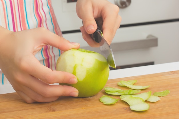 Haciendo un pastel. Chica pela manzanas verdes de la cáscara con un cuchillo en la cocina.