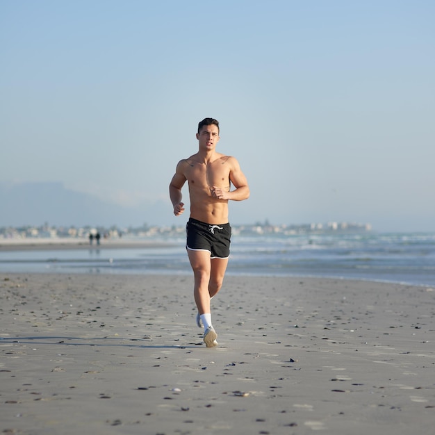 Haciendo pistas Toma de cuerpo entero de un apuesto joven corriendo en la playa