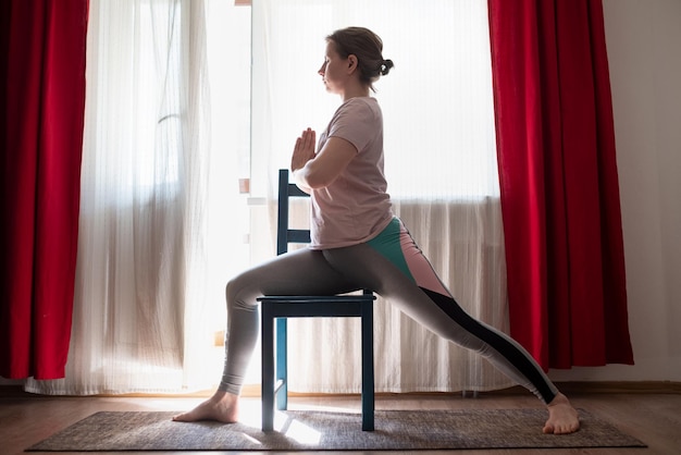 Foto haciendo pose de guerrero virabhadrasana en casa usando una silla