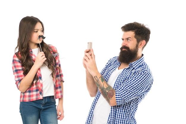 Haciendo recuerdos familiares Un hombre barbudo toma una foto de un niño pequeño Una niña pequeña posa con accesorios de bigote Hipster usa el teléfono móvil Celebración familiar Sesión de fotos familiar La familia lo es todo