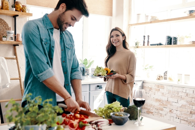 Haciendo todo juntos. Hermosa joven pareja cocinando la cena mientras está de pie en la cocina de casa