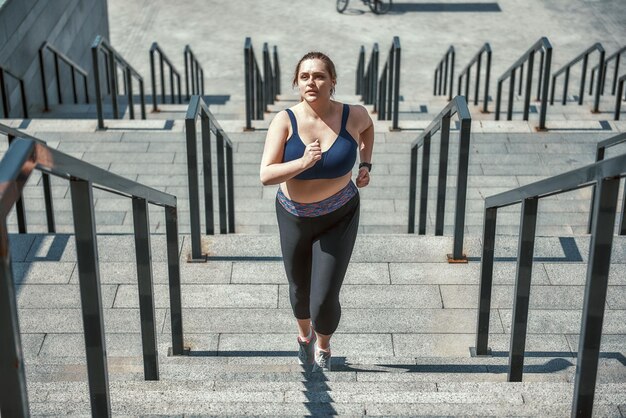 Haciendo todo lo posible. Mujer de talla grande activa en ropa deportiva corriendo por las escaleras mientras hace ejercicio al aire libre