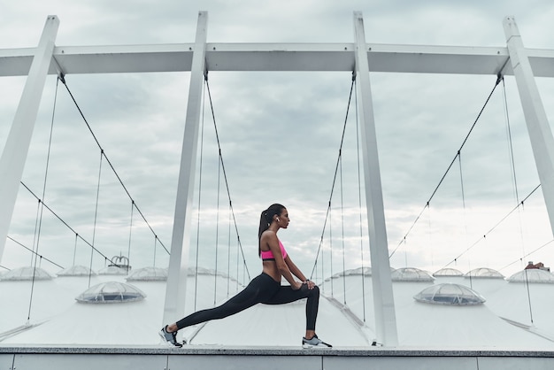 Haciendo yoga. Mujer joven moderna en ropa deportiva que se extiende mientras se calienta al aire libre