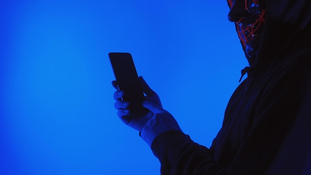 Hacker anônimo de conceito de segurança digital com máscara segurando smartphone hackeado