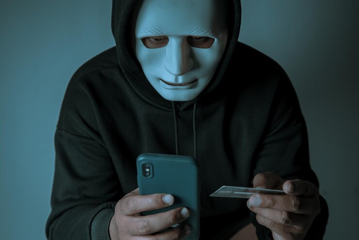 Foto un hacker anónimo enmascarado está usando un teléfono inteligente para penetrar la información financiera de la tarjeta de crédito concepto de piratería y malware