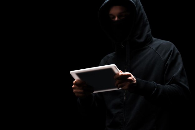 Hacker anônimo no capô usando tablet digital isolado em preto