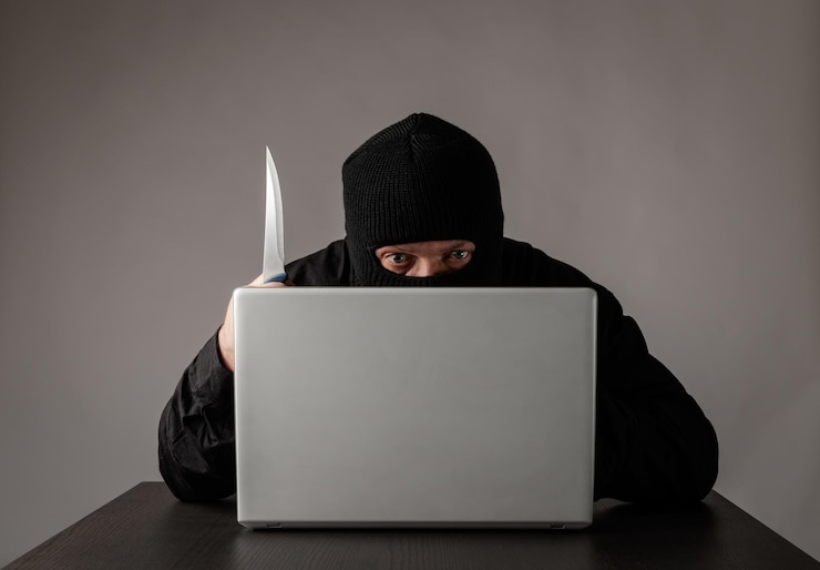 Foto hacker con balaclava usando una computadora portátil contra un fondo gris