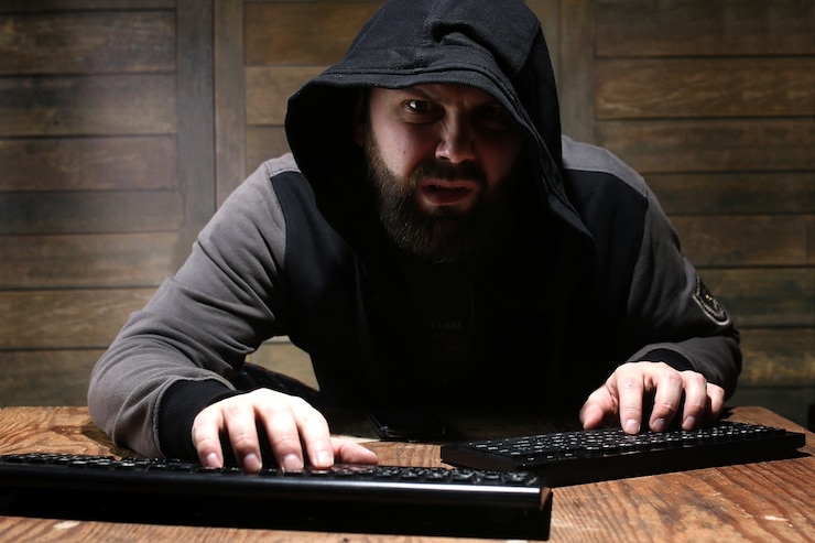 Foto hacker en el capó negro en una habitación con paredes de madera.