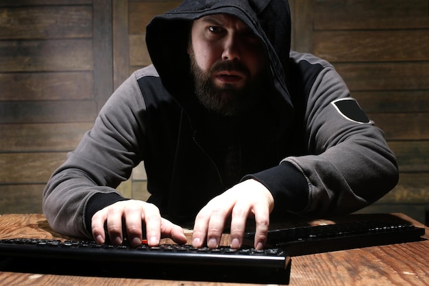 Hacker en el capó negro en una habitación con paredes de madera.