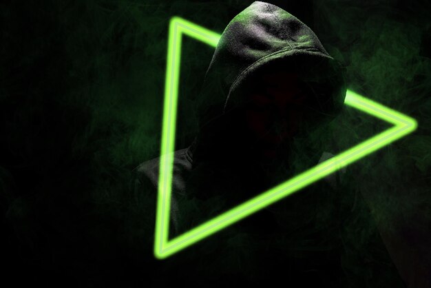 Hacker con capucha lanzando un ciberataque con triángulo de neón verde y humo sobre fondo negro
