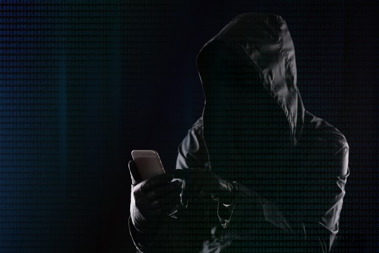 Foto hacker en una capucha oscura piratea un teléfono móvil moderno en el fondo del código binario, concepto de seguridad de datos personales de internet.