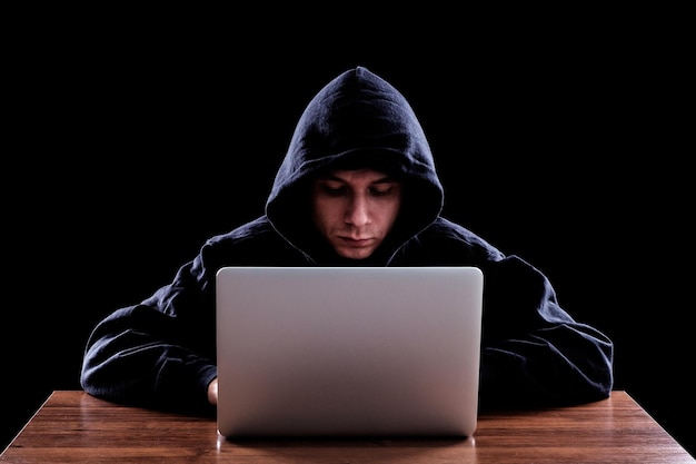 Hacker con una capucha oscura sentado frente a un portátil Concepto de seguridad cibernética Fondo oscuro