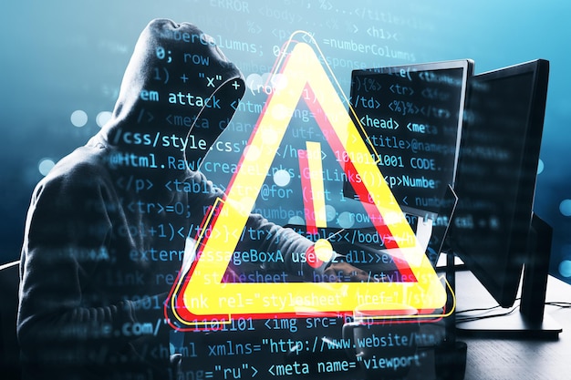 Hacker con capucha trabajando en una computadora con superposición de señales de advertencia digital y código en el fondo