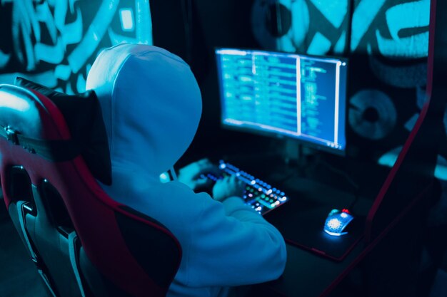 Hacker con capucha trabajando en el sitio del código de hacks en una computadora personal con luz verde