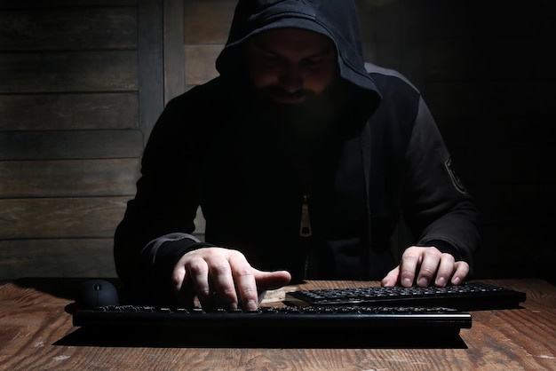 Hacker com capô preto em uma sala com paredes de madeira