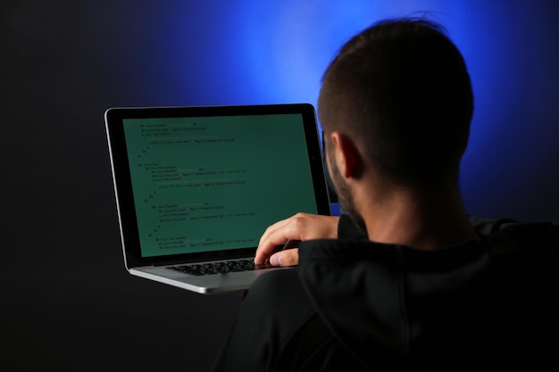 Hacker com computador e laptop em fundo escuro colorido