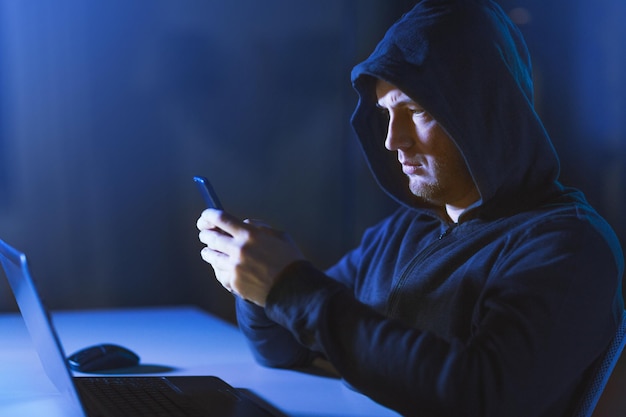 hacker con computadora portátil y teléfono inteligente en una habitación oscura