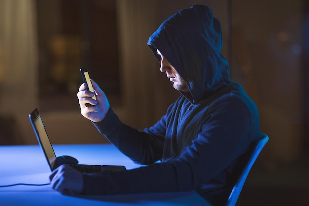 hacker con computadora portátil y teléfono inteligente en una habitación oscura