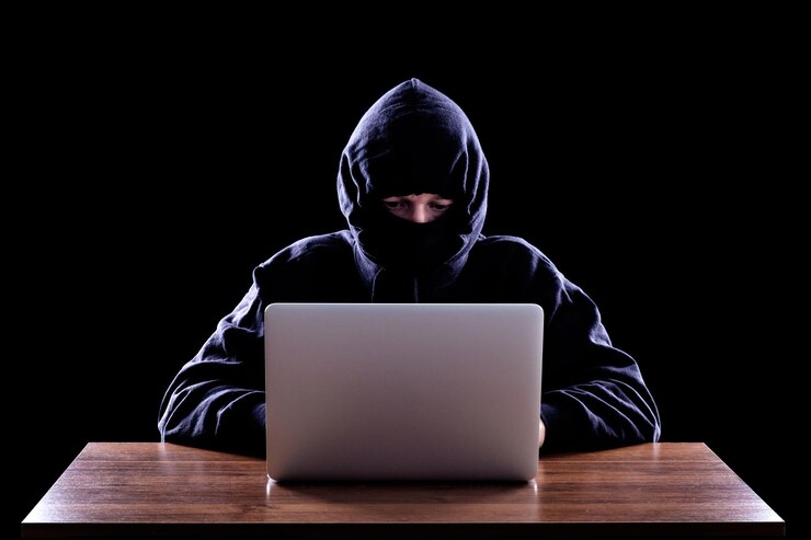 Foto hacker de computadoras con capucha robando información con una computadora portátil fondo oscuro