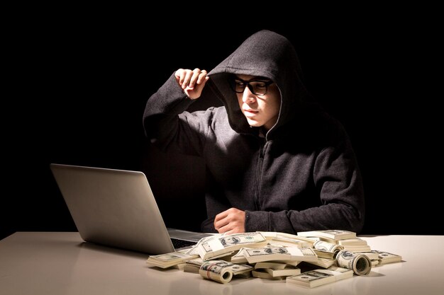 Foto hacker de computador usando laptop por moeda de papel na mesa contra fundo preto