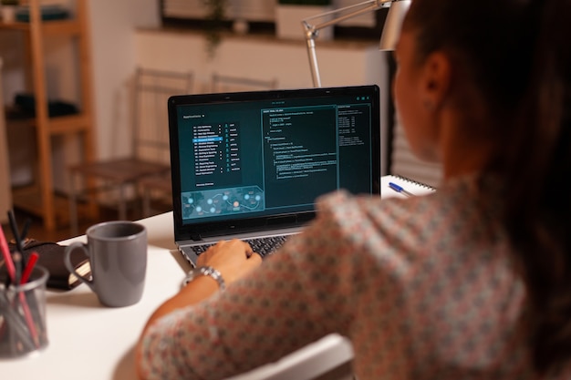 Hacker femenina sentada frente a la computadora y pensando cómo estafar al gobierno por la noche. Programador que escribe un malware peligroso para ataques cibernéticos utilizando una computadora portátil de alto rendimiento durante la medianoche.